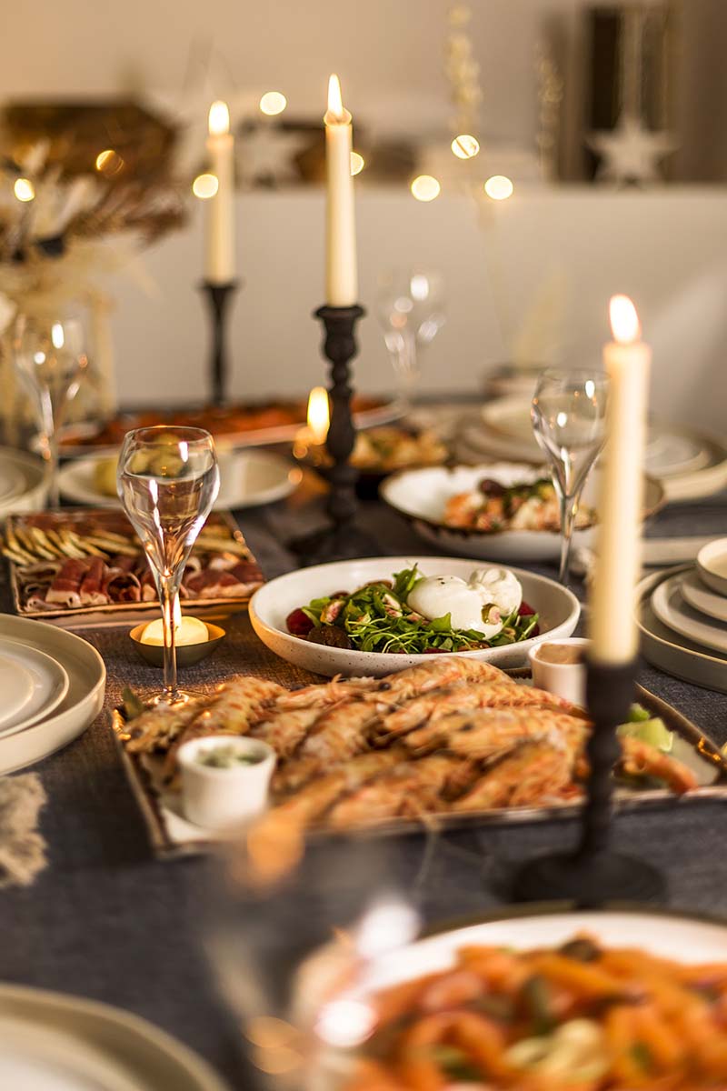 Mesa de Nochevieja con velas, langostinos, ensalada de burrata y jamón ibérico